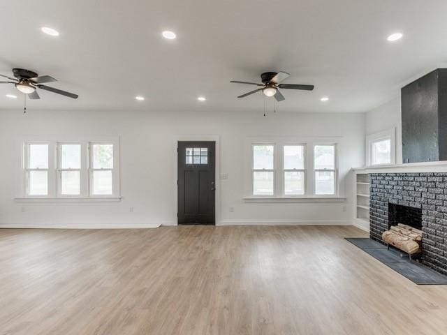 unfurnished living room with wood-type flooring, a wealth of natural light, ceiling fan, and a fireplace