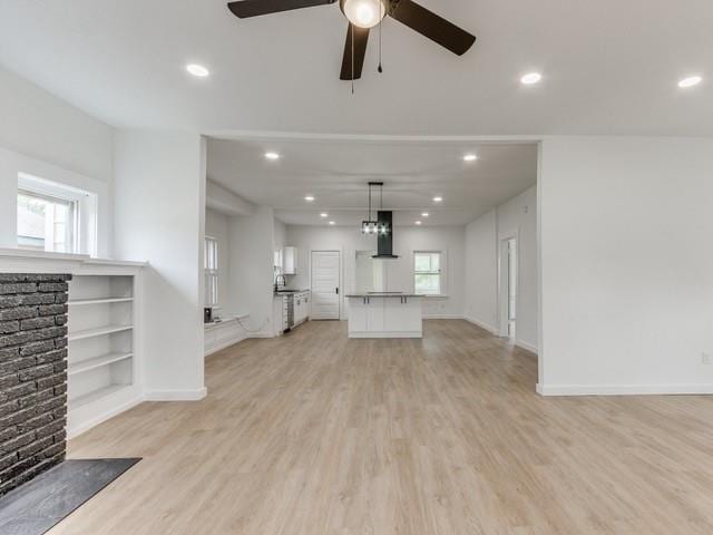 unfurnished living room with built in shelves, plenty of natural light, ceiling fan, and light hardwood / wood-style flooring