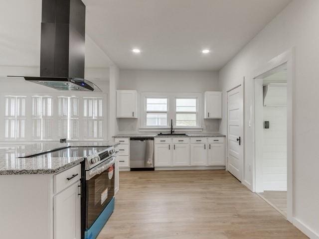 kitchen featuring sink, appliances with stainless steel finishes, wall chimney range hood, light stone countertops, and white cabinets