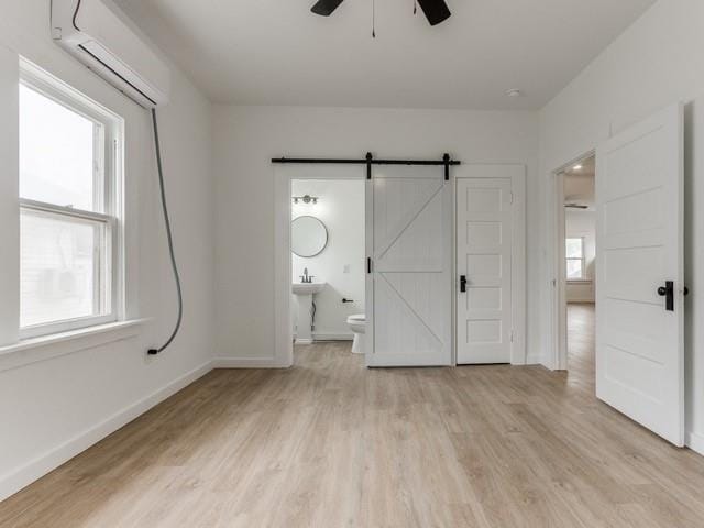 unfurnished bedroom with connected bathroom, multiple windows, ceiling fan, light hardwood / wood-style floors, and a barn door