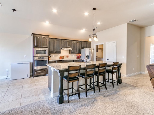 kitchen featuring a breakfast bar area, light stone counters, dark brown cabinets, a large island with sink, and stainless steel appliances