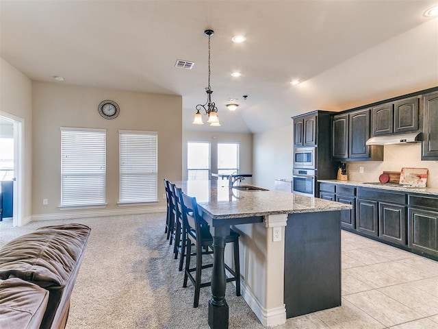 kitchen with light stone countertops, decorative backsplash, stainless steel appliances, and a center island with sink