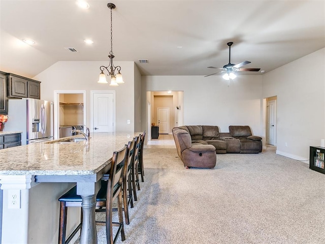 kitchen featuring an island with sink, sink, stainless steel fridge, a kitchen bar, and light colored carpet