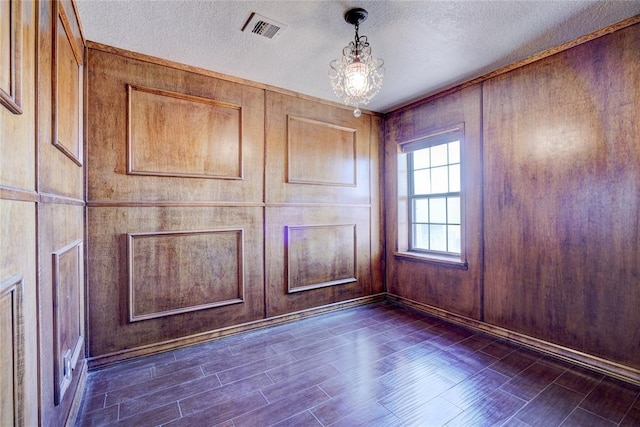 unfurnished room featuring an inviting chandelier, dark hardwood / wood-style floors, wooden walls, and a textured ceiling