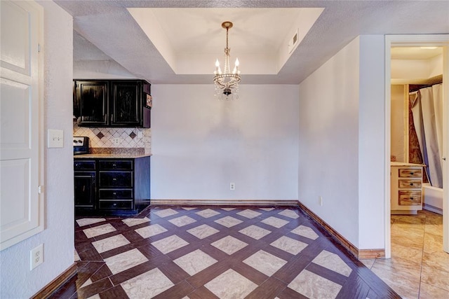 unfurnished dining area featuring a notable chandelier and a tray ceiling