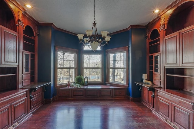 unfurnished dining area with built in shelves, ornamental molding, a chandelier, and a textured ceiling