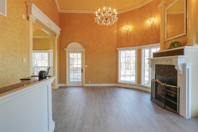 unfurnished living room featuring a notable chandelier, a towering ceiling, a high end fireplace, and wood-type flooring