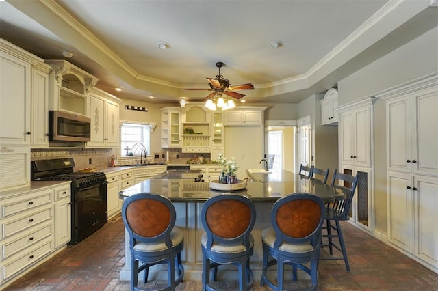 kitchen with a kitchen island, a tray ceiling, gas stove, a kitchen bar, and decorative backsplash