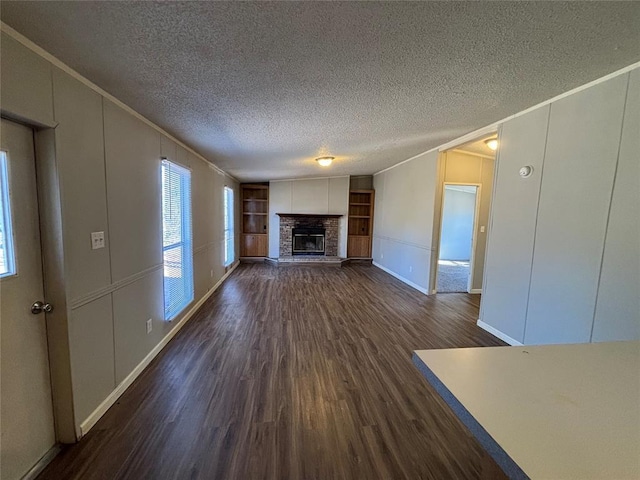 unfurnished living room with built in features, a fireplace, ornamental molding, dark wood-type flooring, and a textured ceiling