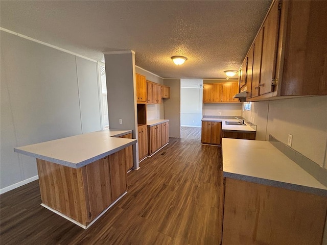 kitchen featuring built in desk, sink, ornamental molding, dark wood-type flooring, and a textured ceiling