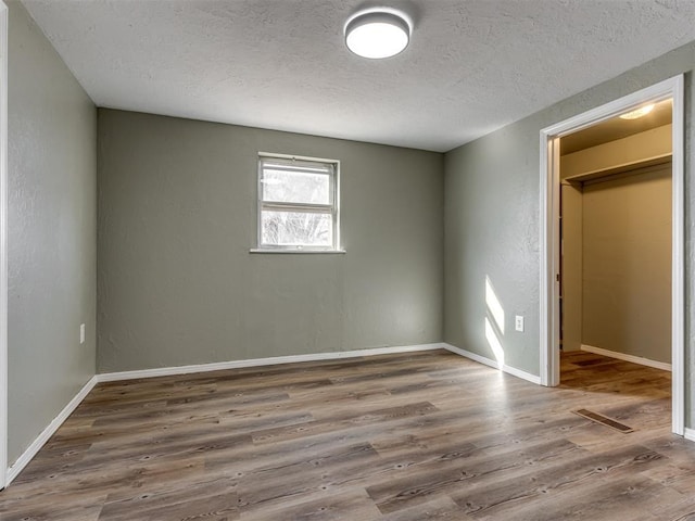 unfurnished bedroom featuring dark wood-type flooring, a walk in closet, a closet, and a textured ceiling