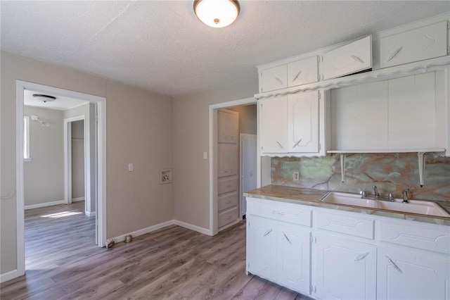 kitchen with tasteful backsplash, white cabinetry, sink, and light wood-type flooring