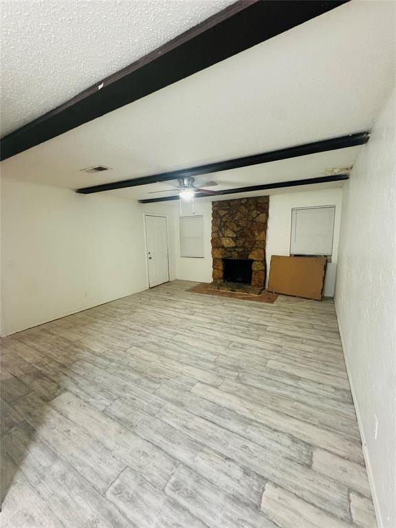 unfurnished living room with beam ceiling, light hardwood / wood-style floors, a stone fireplace, and a textured ceiling