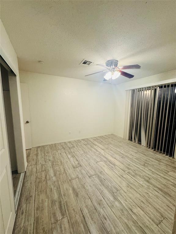 spare room featuring a textured ceiling, light wood-style flooring, visible vents, and a ceiling fan