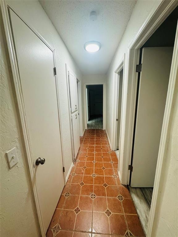 hall with a textured ceiling, a textured wall, and tile patterned floors