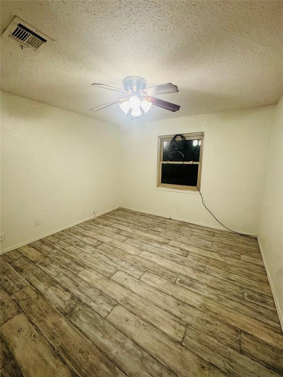 unfurnished room with visible vents, ceiling fan, a textured ceiling, and wood finished floors