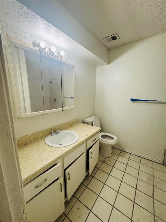 bathroom with visible vents, toilet, vanity, a textured ceiling, and tile patterned floors