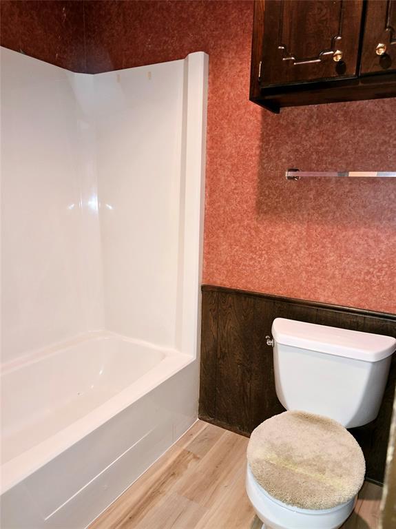 bathroom with hardwood / wood-style floors, toilet, and washtub / shower combination