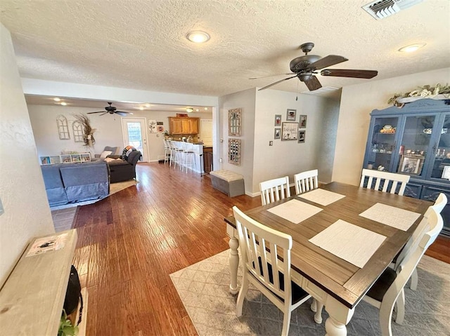 dining space featuring wood-type flooring, ceiling fan, and a textured ceiling