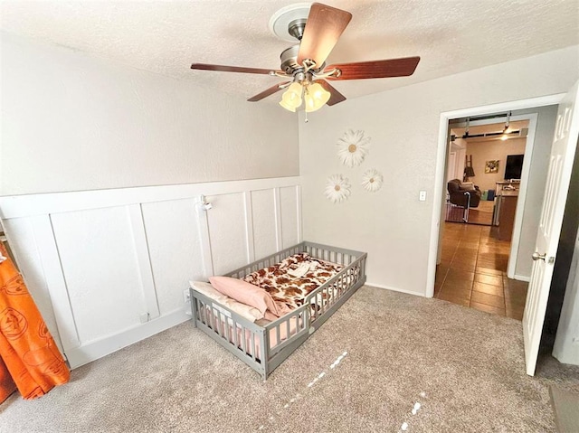 bedroom featuring a textured ceiling, light colored carpet, and ceiling fan