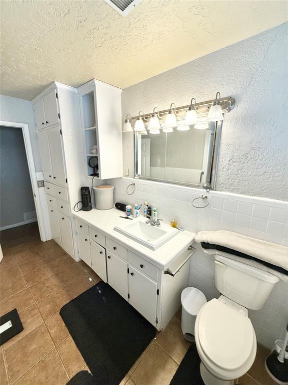 bathroom featuring vanity, toilet, tile patterned flooring, and a textured ceiling