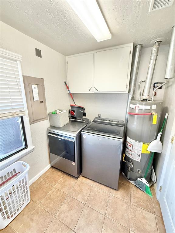 laundry area featuring water heater, cabinets, light tile patterned floors, washing machine and dryer, and a textured ceiling