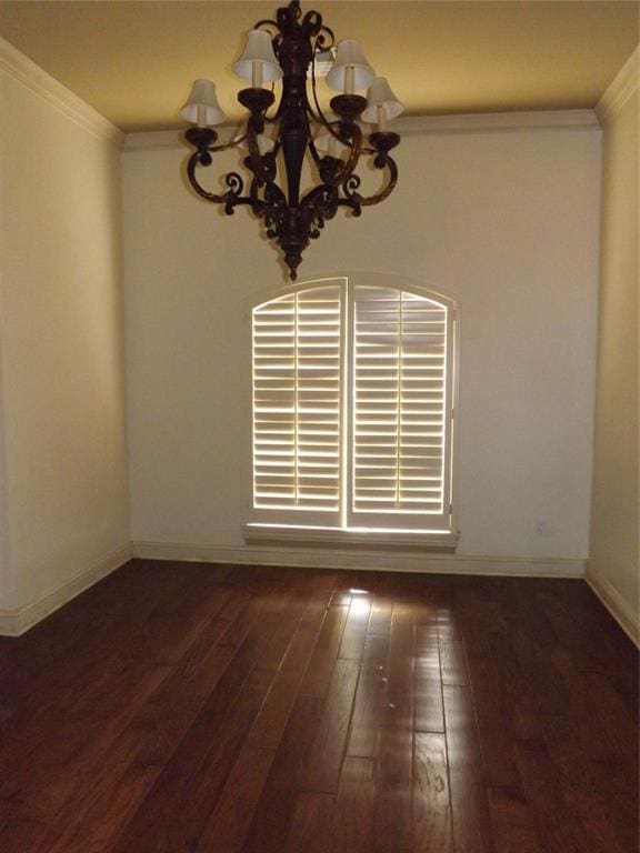 spare room featuring an inviting chandelier, dark wood-type flooring, and ornamental molding