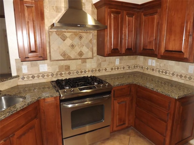 kitchen with light tile patterned floors, stainless steel range with gas stovetop, decorative backsplash, dark stone counters, and wall chimney exhaust hood