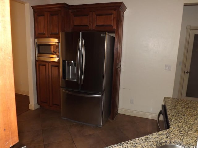 kitchen with appliances with stainless steel finishes, dark tile patterned flooring, and light stone counters