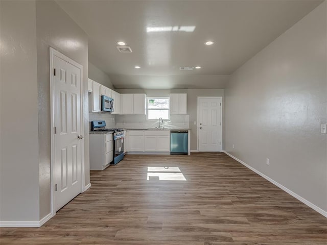 kitchen with backsplash, stainless steel appliances, hardwood / wood-style floors, and white cabinets