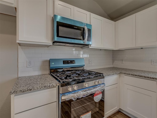 kitchen featuring stainless steel appliances, vaulted ceiling, white cabinets, and light stone counters