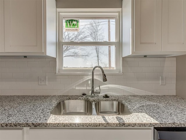 room details with light stone counters, sink, decorative backsplash, and white cabinets