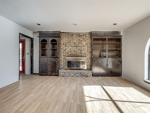 unfurnished living room with a brick fireplace and light wood-type flooring