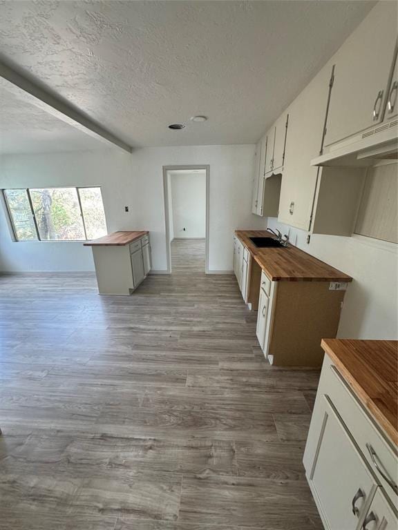 kitchen featuring wood counters, sink, white cabinetry, a textured ceiling, and hardwood / wood-style floors