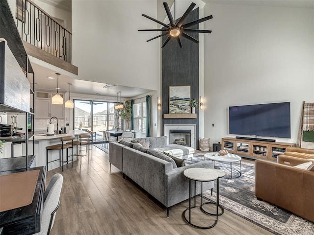 living room with hardwood / wood-style floors, sink, high vaulted ceiling, and a large fireplace