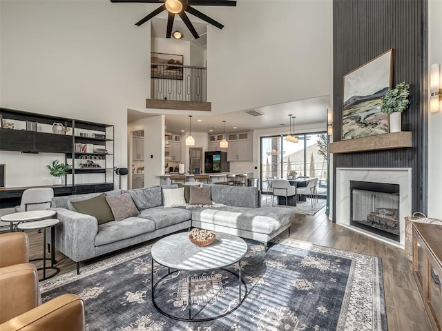 living room featuring a towering ceiling, a fireplace, dark hardwood / wood-style floors, and ceiling fan