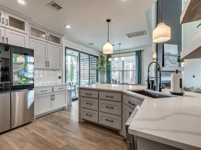 kitchen with pendant lighting, sink, stainless steel refrigerator, light stone counters, and tasteful backsplash