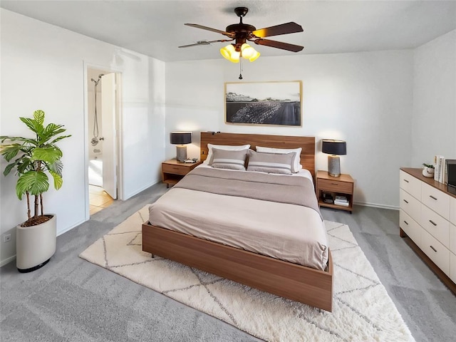 bedroom with ceiling fan, light colored carpet, and ensuite bath