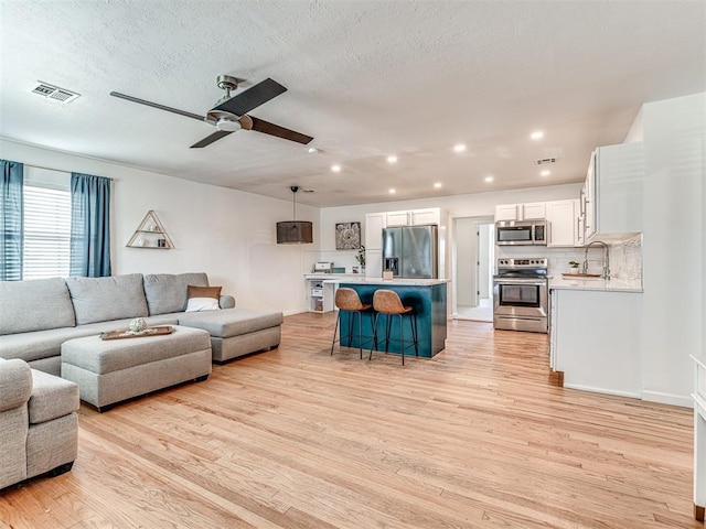 living room with ceiling fan, sink, light hardwood / wood-style floors, and a textured ceiling