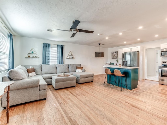 living room featuring ceiling fan, light hardwood / wood-style floors, and a textured ceiling