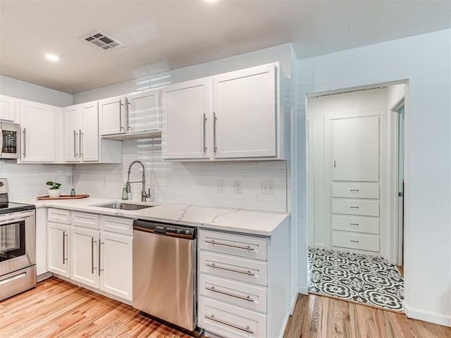 kitchen featuring sink, backsplash, stainless steel appliances, white cabinets, and light wood-type flooring