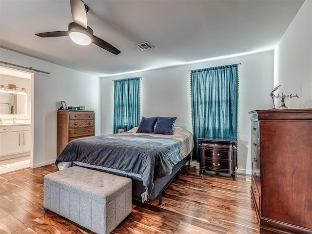 bedroom with a barn door, hardwood / wood-style floors, connected bathroom, and ceiling fan