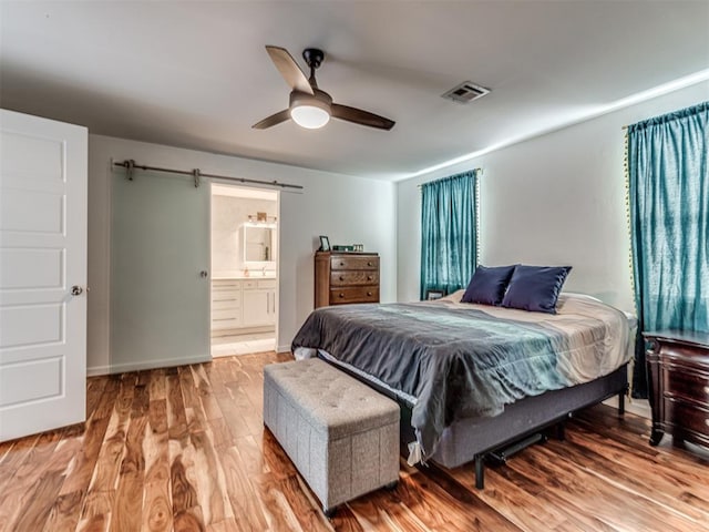 bedroom featuring connected bathroom, hardwood / wood-style flooring, a barn door, and ceiling fan