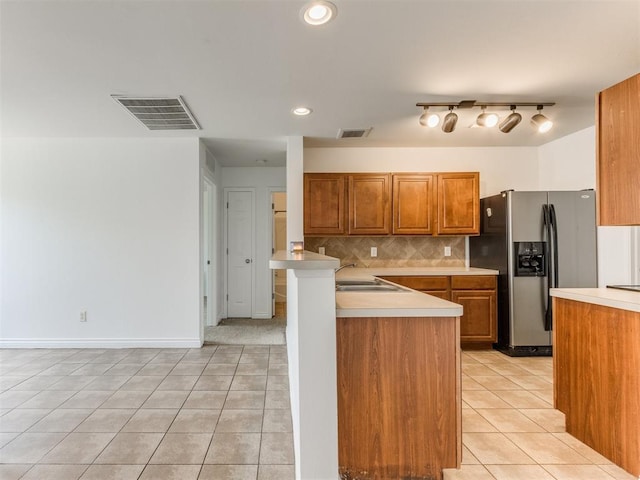 kitchen featuring light tile patterned flooring, stainless steel fridge, kitchen peninsula, and backsplash