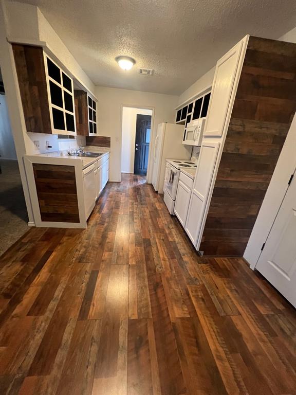 kitchen featuring sink, white appliances, white cabinetry, a textured ceiling, and dark hardwood / wood-style flooring