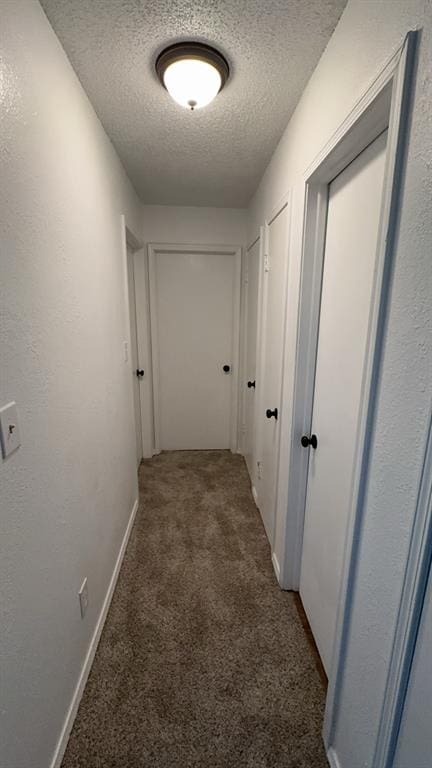 hall with a textured ceiling and dark colored carpet