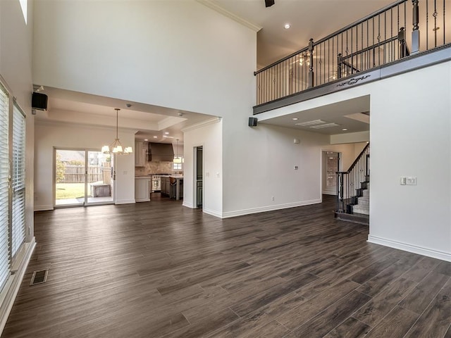 unfurnished living room featuring ornamental molding, dark hardwood / wood-style flooring, a raised ceiling, and a notable chandelier