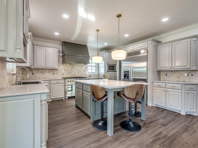 kitchen with sink, hardwood / wood-style flooring, premium range hood, a center island, and built in appliances