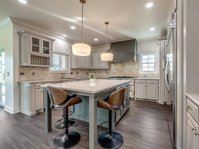 kitchen with gray cabinets, a breakfast bar, decorative light fixtures, custom exhaust hood, and a center island