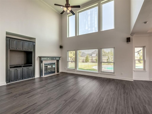 unfurnished living room with crown molding, a towering ceiling, a healthy amount of sunlight, and dark hardwood / wood-style floors